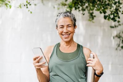Active senior woman holding smartphone and water bottle